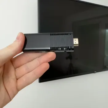 Hand holding HDMI streaming stick in front of TV